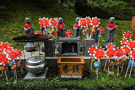 Die Statuen mit den roten Lätzchen im Hintergrund und die Windräder sind ein Zeichen für den Verlust von Kindern oder Föten – auch durch Abtreibung.